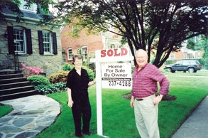 Happy couple who were able to find a for sale by owner home in front of the house standing next to the “sold” real estate sign